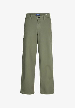 Veste bomber grise claire avec fermeture éclair, portée au-dessus d'un t-shirt blanc, associée à un pantalon vert ample et des baskets noires. Cheveux bouclés.