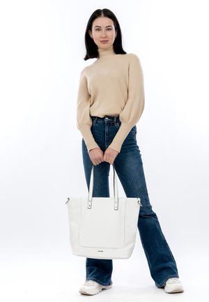 Borsa tote in pelle bianca con doppio manico, texture liscia e design minimalista. Il modello indossa un pullover beige a coste e jeans blu a palazzo.