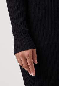 Svart ribbad långärmad tyg med en åtsittande manschett. Texturen är jämn, med subtila vertikala linjer och en ren kant vid handleden.