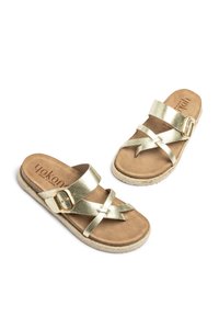 Goldfarbene metallische Rutsch-Sandalen mit Kreuzriemen und einer Schnallendetail. Das Fußbett besteht aus tanfarbenem Wildleder und die Sohle hat einen strukturierten, espadrilleartigen Rand.