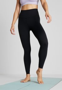 Leggings neri a vita alta realizzati in tessuto elastico, con una texture liscia e un design aderente, adatti per attività sportive.