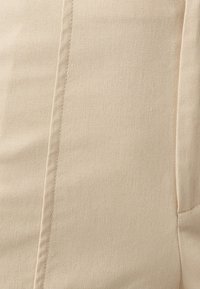 Beige tyg närbild med en subtil textur. Har synliga stygn och en slät yta, vilket indikerar ett lätt material.