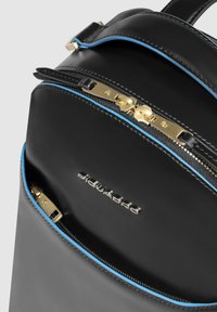 Mochila de cuero negro con cremalleras doradas y detalles en caño azul. Cuenta con dos compartimentos con cremallera y un logo en relieve en el frente.