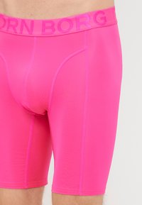 Fuchsiové boxerky s hladkou, lesklou textúrou. Majú elastický pás so značkou "BORN" a zosilneným švom pre väčšiu odolnosť.