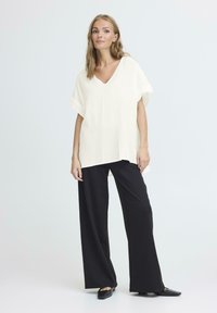 Top bianco con texture a V abbinato a pantaloni neri a gamba larga. Il top presenta maniche corte, creando una silhouette rilassata.