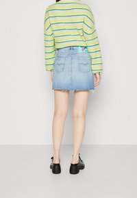 Džínová mini sukně s třepeným lemem, má dvě zadní kapsy. Nosit s pruhovaným pleteným svetrem zelené a žluté barvy.