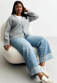Grå cardigan med knappframsidan, buren över en vit t-shirt. Kombinerad med vida, ljusblå jeans med en slitna fåll. Vita sneakers.