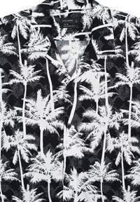 Camicia a maniche corte bianca e nera con motivo di palme. Vestibilità comoda con colletto e dettagli con bottoni anteriori.