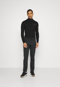 Black zippered long-sleeve top, slim-fit gray trousers, and black sneakers with brown accents; smooth material, minimalist branding.