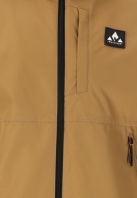 Beige jacka med svart dragkedja, som har en framficka och en logotypapplikation. Slät textur, lättviktig material, lämplig för utomhusbruk.