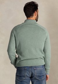 Lichtgroene pullover trui met een gestructureerd breipatroon, voorzien van een hoge kraag en raglanmouwen, gecombineerd met blauwe denim jeans.