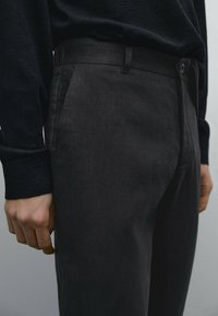 Black, slim-fit trousers made of textured fabric with a smooth finish, featuring side pockets and a discreet waistband.