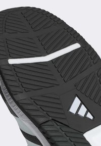Semelle de chaussure en caoutchouc noir avec un motif de traction texturé, présentant une ligne d'accent blanc et une découpe triangulaire dans le design.
