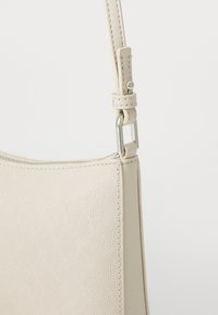 Borsa a tracolla sintetica beige con motivo geometrico embossato, caratterizzata da una texture liscia e un attacco per cinturino in metallo argentato.