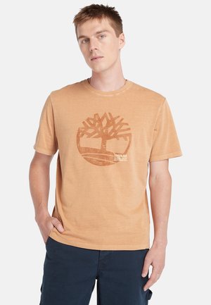 Light orange cotton t-shirt featuring a brown tree silhouette graphic with text. Short sleeves and a crew neckline.
