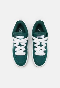 Vihreät tennarit valkoisilla nauhoilla ja tehosteilla, joissa on pehmustettu kaulus, pyöreä kärki ja näkyvä "PUMA"-brändäys kielekkeessä.