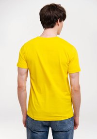 Gelbes Baumwoll-T-Shirt mit Rundhalsausschnitt, kurzen Ärmeln und glatter Textur, kombiniert mit blauen Jeans im Denim-Stil mit auffälligen Gesäßtaschen.