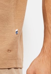 Bruine katoenen T-shirt met een zijlabel met blauwe, witte en marine strepen; zachte textuur; gestikt logo-detail nabij de zoom.