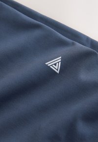 Gros plan d’un tissu bleu marine avec un petit logo triangulaire géométrique blanc imprimé sur la surface.