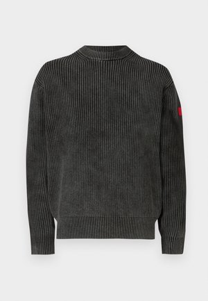 Temno sivi rebrasti pulover z visokim ovratnikom, dolgimi rokavi in majhnim rdečim poudarkom na levem rokavu. Teksturirana tkanina z vertikalnimi črtami.