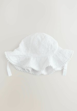 Weißer Baumwollsonnenhut mit einem floralen Lochmuster, breiter Krempe, Quastenverzierung und verstellbaren Bindebändern an den Seiten.