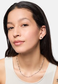 Zilveren studoorbellen met een ronde vorm en een matte afwerking. Een zilveren schakelketting wordt gedragen en past mooi bij een lichtbeige top.