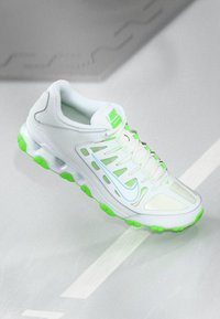 Weißer Sportschuh mit einem Mesh-Obermaterial, grünen Gummielementen an der Sohle und einem hellblauen Swoosh-Logo. Verfügt über ein Schnürdesign.