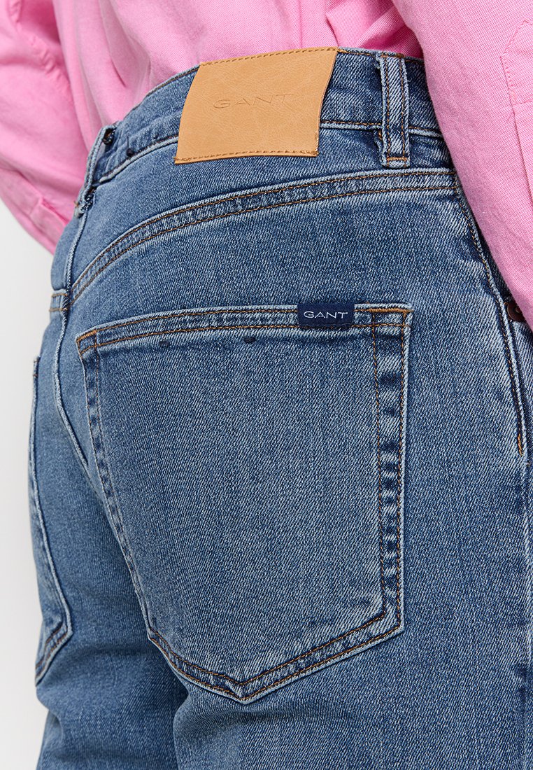 Jeans de denim azul con un parche de cuero GANT en la cinturilla y una etiqueta azul en el bolsillo trasero. Presentan costuras sutiles y un corte clásico.