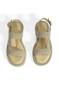Beige suède sandalen met twee brede banden over de voet, een achterband en een gevoerde binnenzool. Gouden hardwareaccent op de achterband.