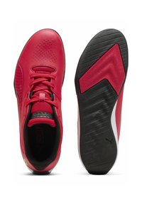 Zapatillas deportivas rojas con parte superior de cuero liso, detalles perforados, suela negra plana y acentos texturizados en el talón y la suela.