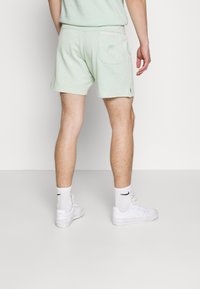 Mintgrüne Baumwollshorts mit einer Gesäßtasche, Logodetails und seitlichen Schlitzen, kombiniert mit weißen Socken und Sneakers.