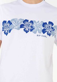 Hvid t-shirt med et horisontalt mønster af blå og lyseblå hibiscusblomster. "RIP CURL" tekst i blå nederst i midten.