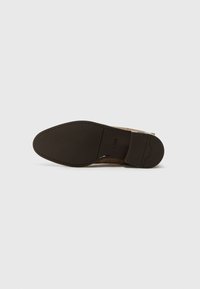 Semelle en cuir brun avec une texture lisse, forme arrondie et un léger talon. Présente un logo près du talon et des détails de couture.