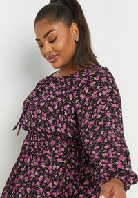 Svart blommig klänning med rynkad hals, elastisk midja och långa ärmar med volangfåll. Små rosa och lila blommor över hela klänningen.