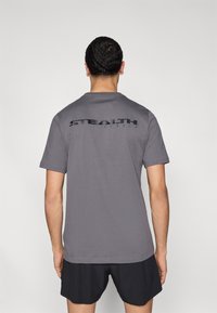 Γκρι βαμβακερό t-shirt με κοντά μανίκια, με μαύρο τυπωμένο λογότυπο "STEALTH RUBBER" στην πάνω πλάτη. Λείο ύφασμα.