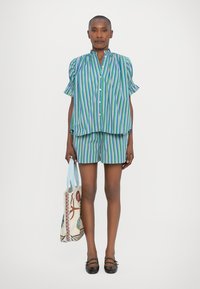Camisa de algodón a rayas en azul, verde y púrpura con mangas cortas abullonadas; pantalones cortos a juego; sosteniendo un bolso de mano estampado; bailarinas negras.
