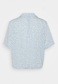 Camicetta a maniche corte di colore azzurro chiaro con un motivo floreale caratterizzato da piccoli fiori bianchi e foglie verdi. Vestibilità comoda e design con colletto.