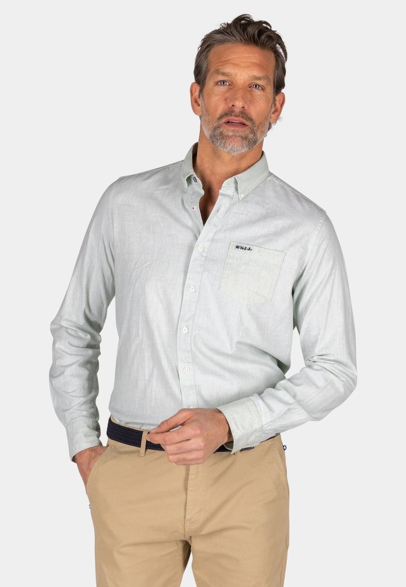 Lichtblauwe blouse met lange mouwen en knoopsluiting, textuurstof, borstzak en geborduurd logo, gecombineerd met beige broek.