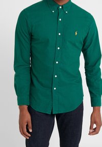 Camisa verde de algodón con cuello de solapa, mangas largas y un pequeño logotipo bordado en el pecho.