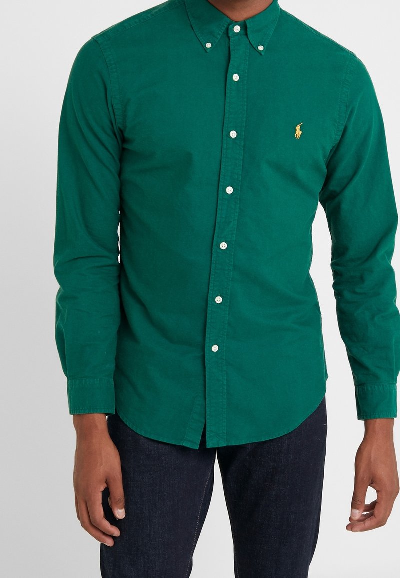 Camisa verde de algodón con cuello de solapa, mangas largas y un pequeño logotipo bordado en el pecho.