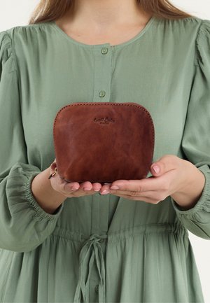 Pochette en cuir marron avec des bords arrondis et une surface texturée, dotée d'une fermeture éclair et d'un logo en relief sur le devant, tenue dans deux mains.