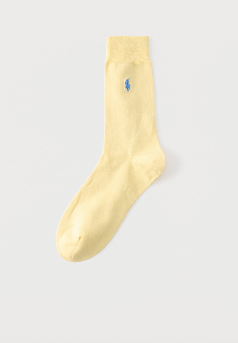 Ένα μοναδικό ανοιχτό κίτρινο καλτσάκι με ραβδωτό μανσέτα και μικρό μπλε κεντημένο λογότυπο παίκτη πόλο κοντά στην κορυφή πάνω σε μονόχρωμο φόντο.