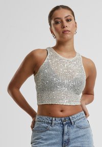 Stříbrný crop top s flitry a ribbovanou texturou, s kulatým výstřihem a bez rukávů, v kombinaci s džíny s vysokým pasem.