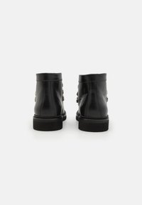 Bottines en cuir noir avec une texture lisse, présentant un petit talon empilé, des boucles latérales et une tige arrondie.