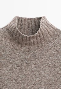 Bruine gebreide coltrui met een geribbelde kraag, textuurpatroon en zachte, warme stof.