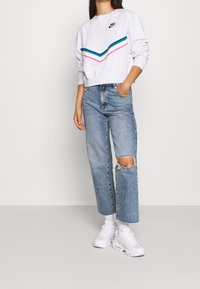 Harmaa cropattu huppari, jossa on monivärinen viivakuosi, yhdistettynä vaaleansinisiin korkeavyötäröisiin farkkuihin, joissa on polvi-reikä ja valkoiset tennarit.