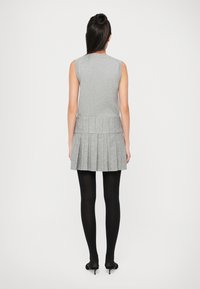 Abito grigio senza maniche con gonna plissettata, tessuto strutturato e corpino aderente. Indossato con collant neri e tacchi, visto da dietro.