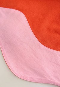 Baumwollstoff in zwei Abschnitten: leuchtendes Orange und zartes Pink, mit einem geschwungenen Nahtdesign, glatter Textur und sauberem Stich.