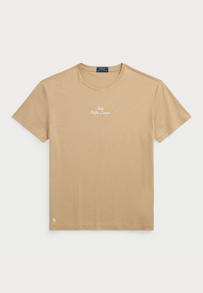 Beige bomulls T-skjorte med rund hals, korte ermer, og "Polo Ralph Lauren" brodert i hvitt på brystet. Har en liten logo ved kanten.