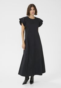 Črna maksi obleka z nabranimi korte rukavi, ki ima ravno rez in šivne detajle, v kombinaciji z elegantnimi črnimi gležnjarji.